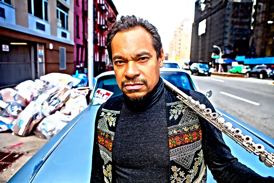 Jay Rodriguez Sierra holding a flute beside a blue car on a New York street.
